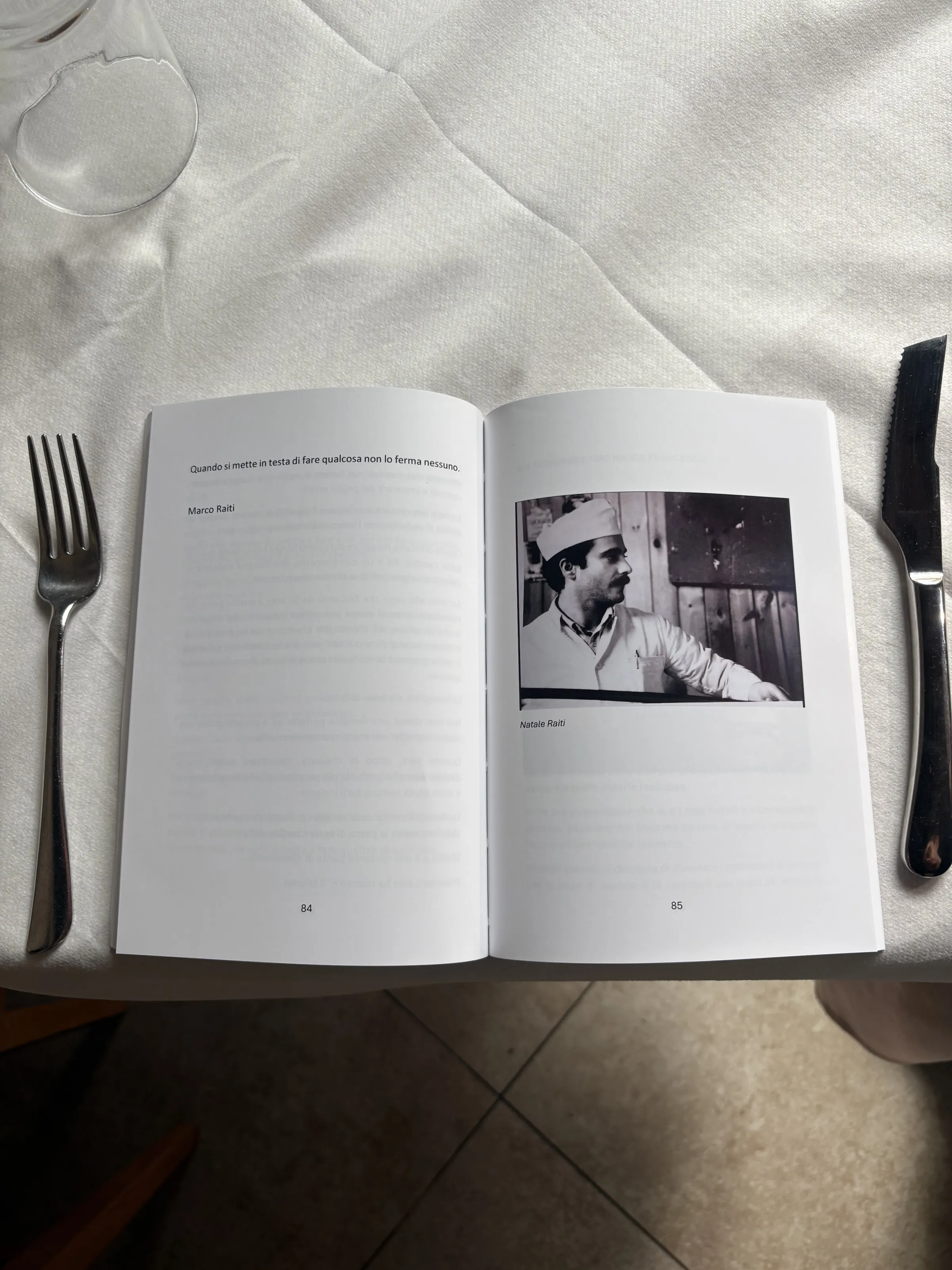 Il libro 'I primi 50 anni dell'Este Bar' aperto su un tavolo apparecchiato di Estebar, con la foto in bianco e nero di Natale Raiti giovane