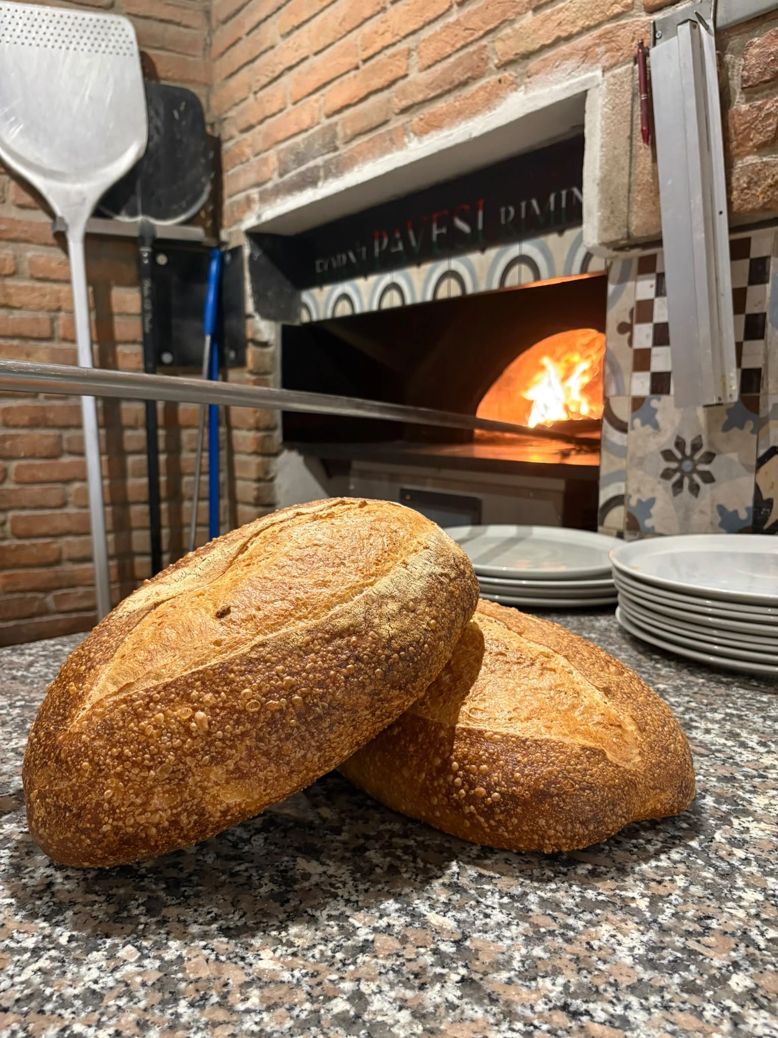 Pane fresco appena sfornato sul bancone di Estebar, con il forno a legna acceso sullo sfondo